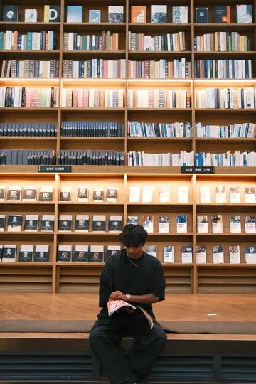 Me reading on a bench under a wall of bookshelves.