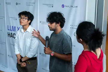 Me with a microphone presenting at the Hack the Law hackathon in Cambridge, a teammate beside me.