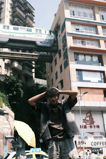Me with my hands on my head in the street while a monorail train runs through the middle of a tower block behind me.