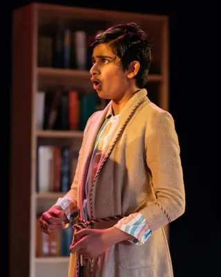 Me on stage in a school play, mid-line, in a long coat against a dark set.