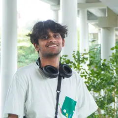 Sanay smiling under a covered walkway, headphones round his neck.