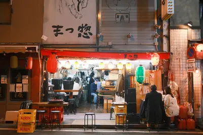 A small restaurant in Japan at night, its front open to the street, red lanterns over the counter.