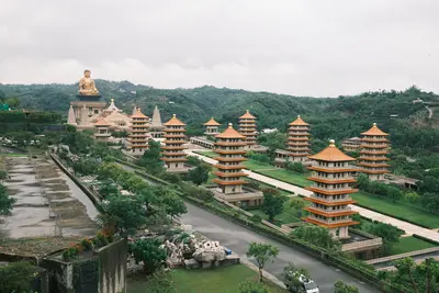 Rows of pagodas leading to a large seated Buddha on a green hillside.