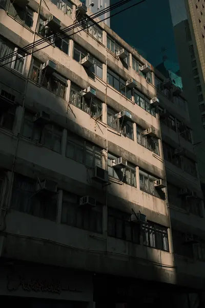 The side of an old apartment block in hard afternoon light, air conditioners on every floor.