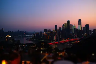 A city skyline at blue hour across a river, the towers and a bridge lit up.
