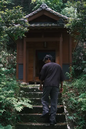 Me climbing mossy stone steps to a small wooden shrine in a forest.